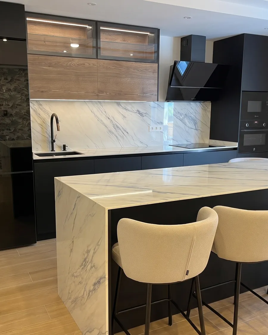 Cocina negra con isla de porcelánico en cascada y taburetes tapizados