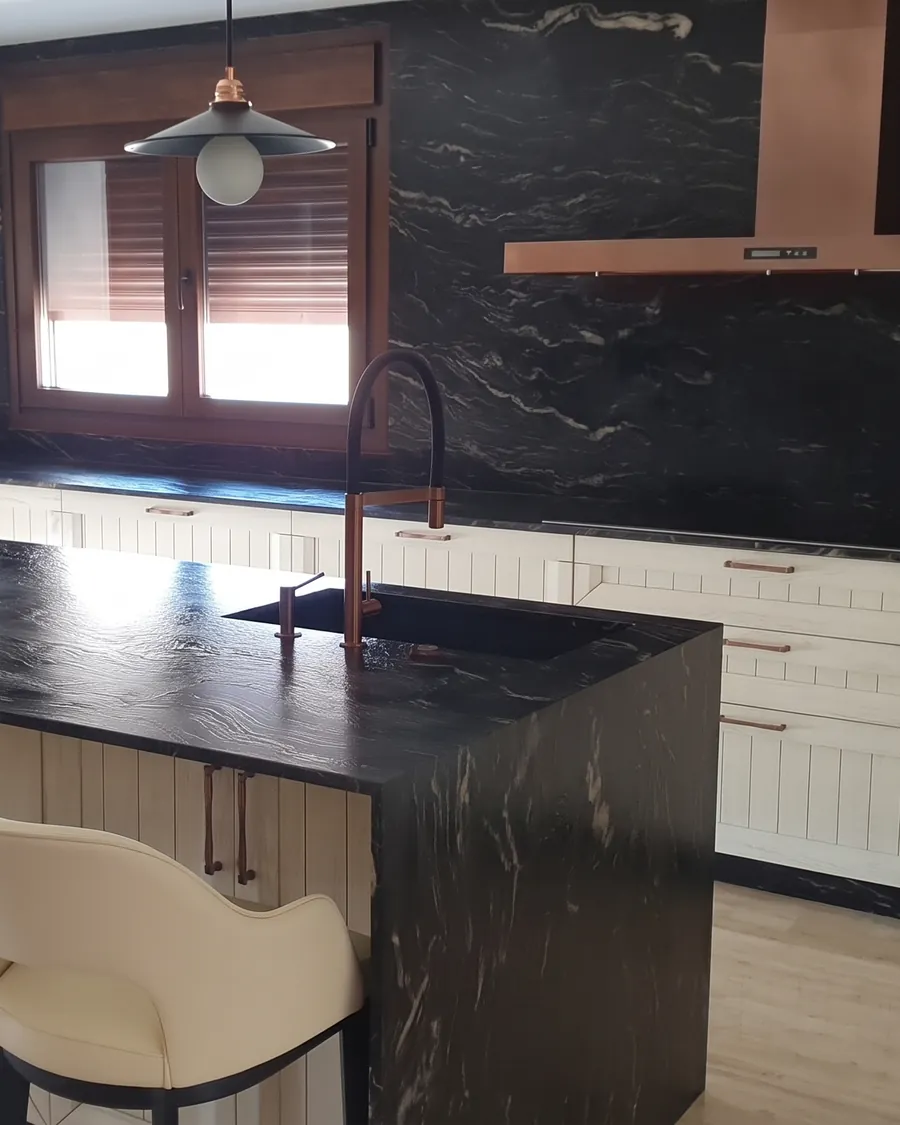 Cocina blanca con isla de piedra negra veteada y campana de cobre